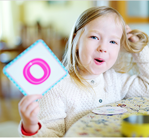 Little girl holding up 'O' Flashcard